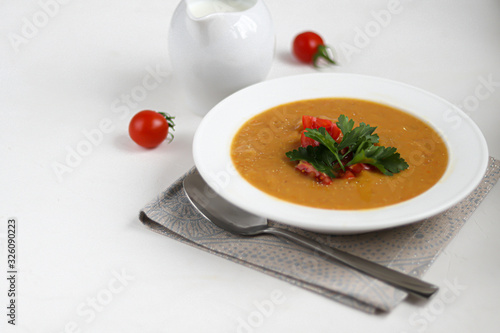 Vegetable soup with lentils on a white background. Served with chopped cherry tomatoes and herbs. Nearby are pieces of ciabatta. Raw groats in the background. Vegetarian dish.