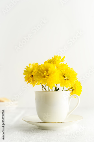 Small bouquet of yellow spring flowers in white cup. Closeup view