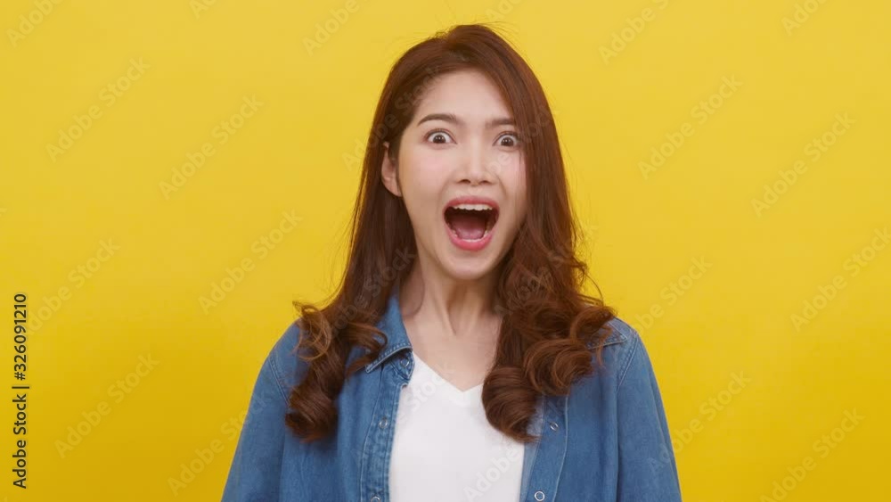 Portrait young Asian lady with positive expression, joyful surprise funky, dressed in casual cloth and looking at camera over yellow background. Happy adorable glad woman rejoices success. Slow motion Portrait young Asian lady with positive expression, joyful surprise funky, dressed in casual cloth and looking at camera over yellow background. Happy adorable glad woman rejoices success. Slow motion