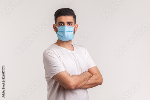 Effective protection against coronavirus. Man holding hands crossed and wearing hygienic mask to prevent infection, respiratory illness such as flu, 2019-nCoV. indoor studio shot, white background