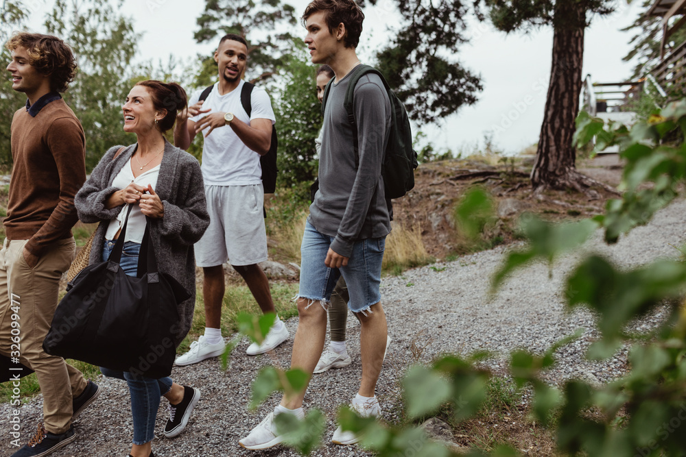 Smiling friends and family walking on footpath amidst trees during vacation Smiling friends and family walking on footpath amidst trees during vacation