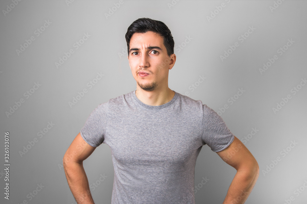 handsome man in grey t-shirt having doubts looking directly to the camera handsome man in grey t-shirt having doubts looking directly to the camera