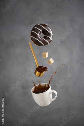 a cup of coffee with a splash freezes in the air a coffee spoon hovering in the air pours out coffee falling pieces of sugar overhang a white striped chocolate donut