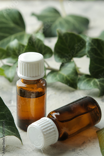 A leaf of ivy and syrup in a bottle on a light concrete table. Production of cough medicine with ivy extract. pharmaceutical industry