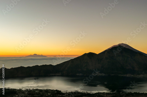 A morning golden hour seen from top of Mount Batur on Bali  Indonesia. There is Mount Rinjani in the back  Lombok  and Volcano Agung on the side. Fog in the valley. Mysterious and magical sunrise.