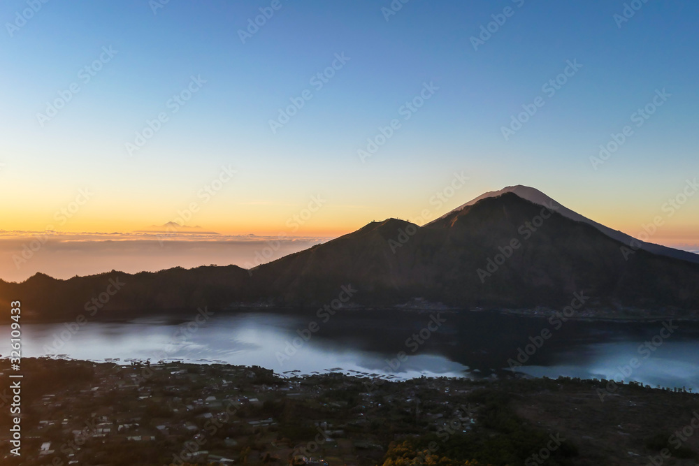 A morning golden hour seen from top of Mount Batur on Bali, Indonesia. There is Mount Rinjani in the back (Lombok) and Volcano Agung on the side. Fog in the valley. Mysterious and magical sunrise.