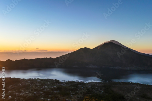 A morning golden hour seen from top of Mount Batur on Bali  Indonesia. There is Mount Rinjani in the back  Lombok  and Volcano Agung on the side. Fog in the valley. Mysterious and magical sunrise.