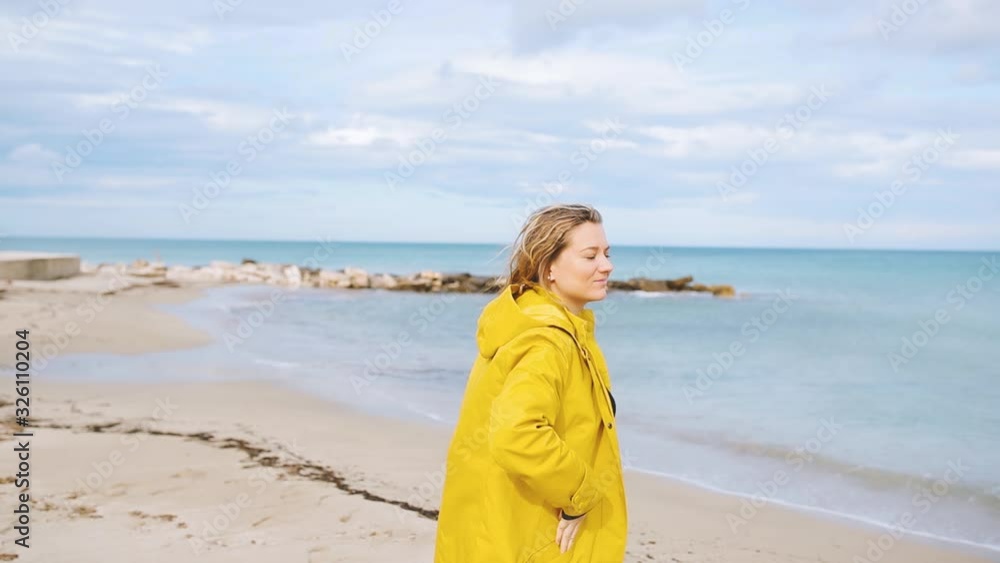 Blond Beautiful woman in Yellow Jacket walk throught the beach. Wind and cloudy wheather Blond Beautiful woman in Yellow Jacket walk throught the beach. Wind and cloudy wheather