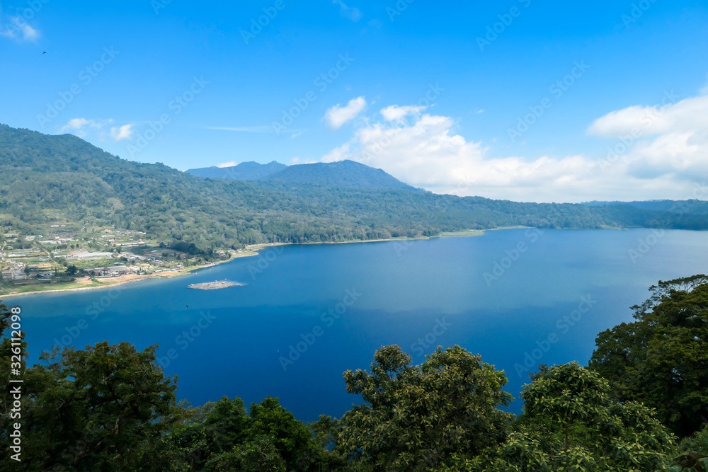 A panoramic view on The Twin Lake, Bali, Indonesia. The lake is surrounded by lush green plants. There are small hills all around the lake. Touristic attraction. Biggest lake on Bali