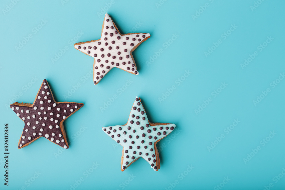 Obraz premium Close-up of three homemade glazed gingerbread cookies made in the form of stars on a blue background. Handmade cookies. Free space.