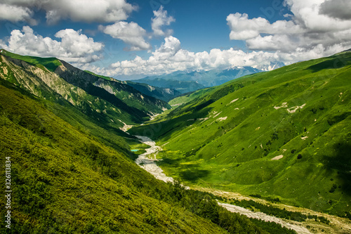 Stunning Adishi valley summer landscape seen from Chkhutnieri pass  Upper Svaneti  Georgia. Vibrant green slopes of Caucasus mountani range on a partially cloudy day.