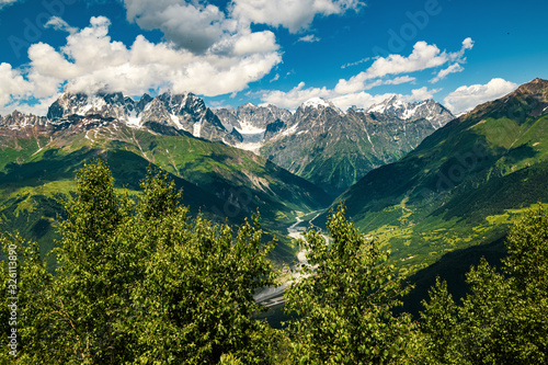 View of the Mestia valley on a summer afternoon shot through the trees with Caucasus mountains in the backgroud.