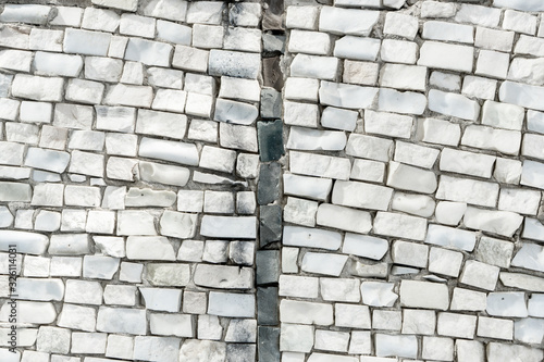 surface of old crumbling abstract decorative mosaic. White ceramic stones on wall are divided into two parts by black tiles. geometric background for your design with copy space and place for text