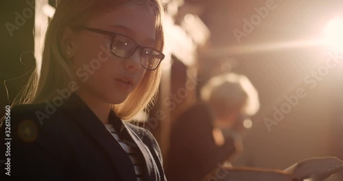 Close up of small Caucasian blond girl in glasses reading old book in dark library with magical atmosphere. Cute schoolgirl studying with texbook in passage with books. Od librarian on background. photo