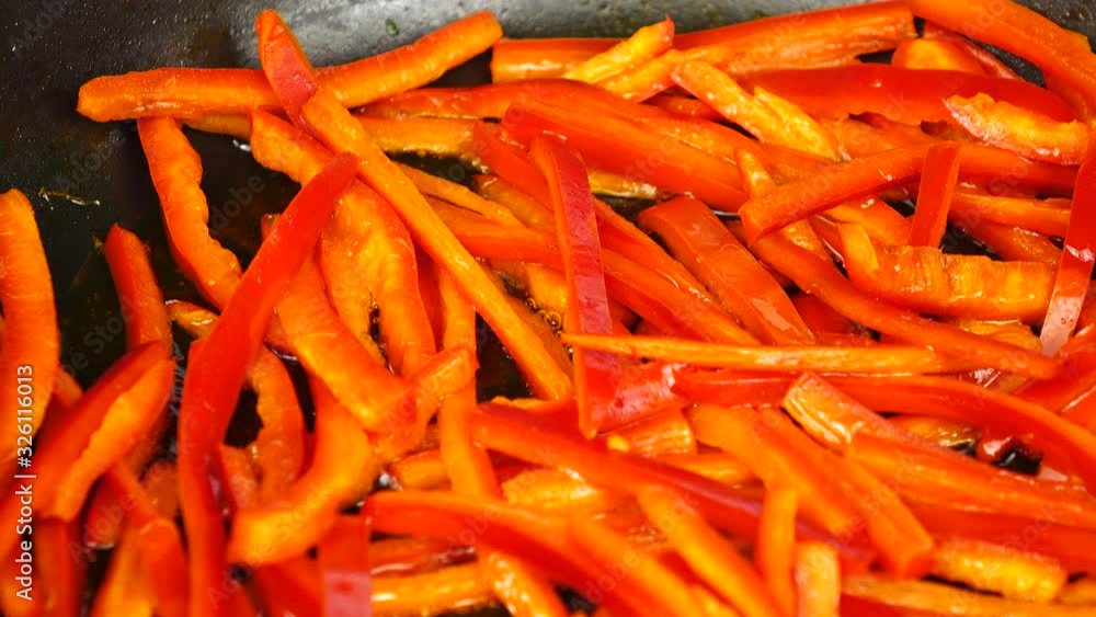 Thin slices of red sweet pepper are sautéing in a black frying pan on a white background Thin slices of red sweet pepper are sautéing in a black frying pan on a white background
