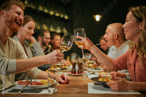 Best friends sitting in restaurant for dinner and making a toast with white wine. On table is food.