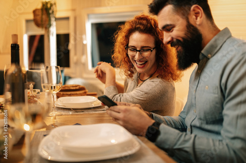 Happy couple using smart phone at dining table.