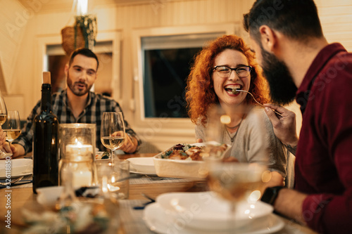 Cheerful woman having fun while being feed by her boyfriend at dining table.