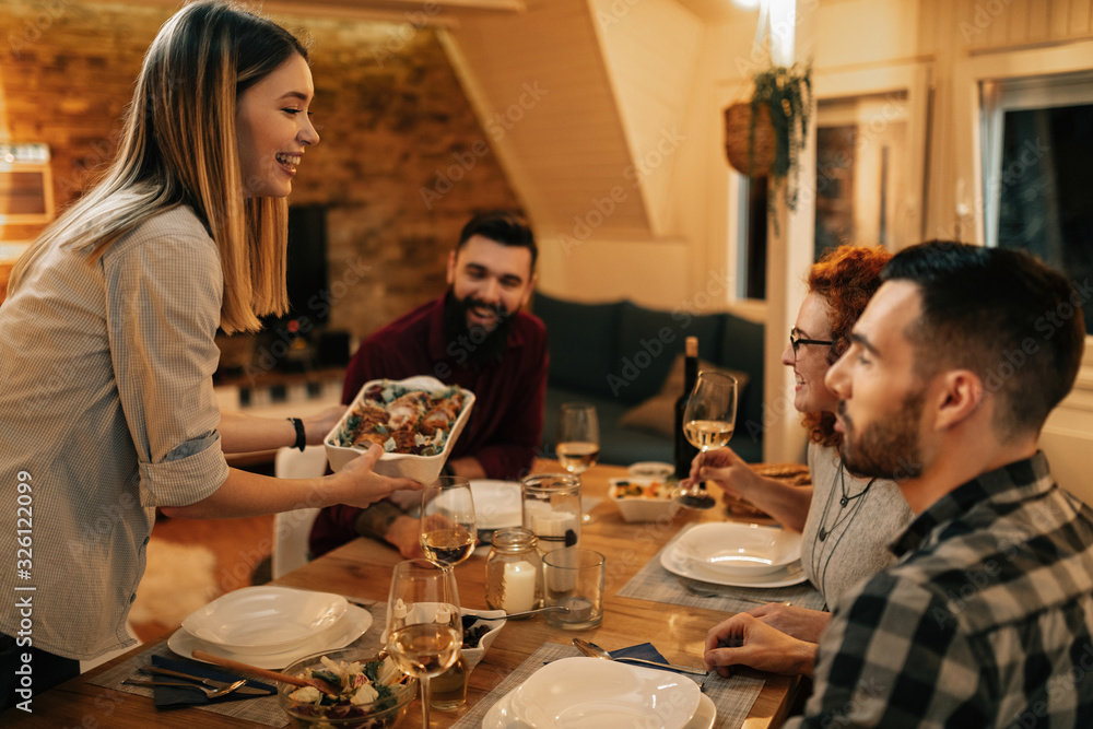 Happy woman bringing food to the table while having dinner with friends. Happy woman bringing food to the table while having dinner with friends.