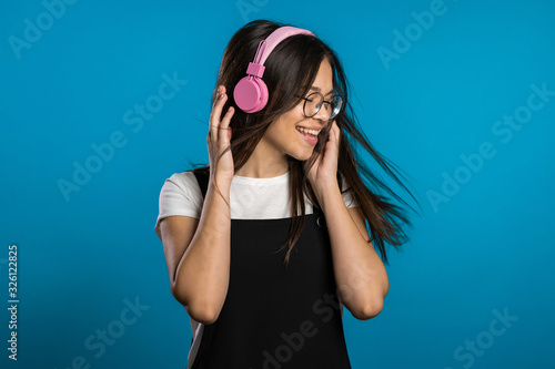 Pretty young asian girl with long hair having fun, smiling, dancing with headphones in studio against blue background. Music, dance, radio concept,