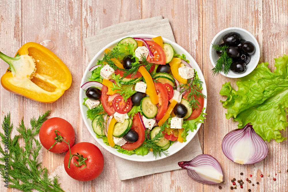 Greek salad with cucumeber, olives, feta cheese, cherry tomatoes, bell pepper, onion and lettuce. Diet, vitamin food. Healthy vegetarian meal concept. Tasty salad in bowl on wood, top view.