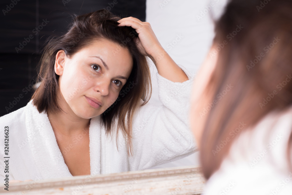 Naklejka premium portrait of a girl looking at herself in the reflection of the mirror, with disheveled hair. Greasy, dirty hair.