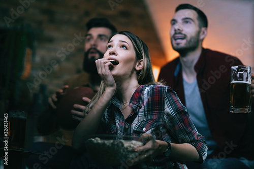 Excited woman and her friends watching sports match on TV at home.