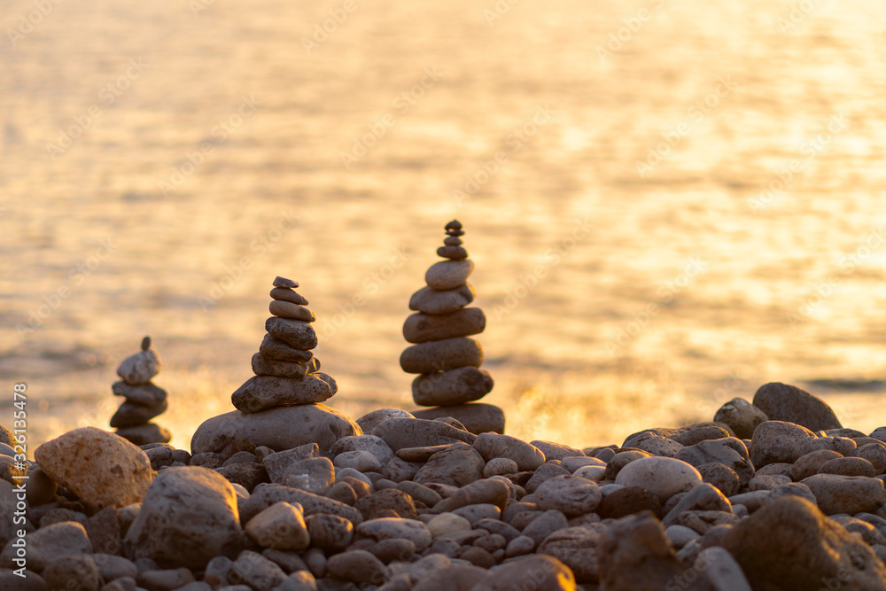 Balanced stone pyramide on shore of the ocean at dawn. Sea pebbles tower closeup symbolizing stability, zen, harmony, balance.