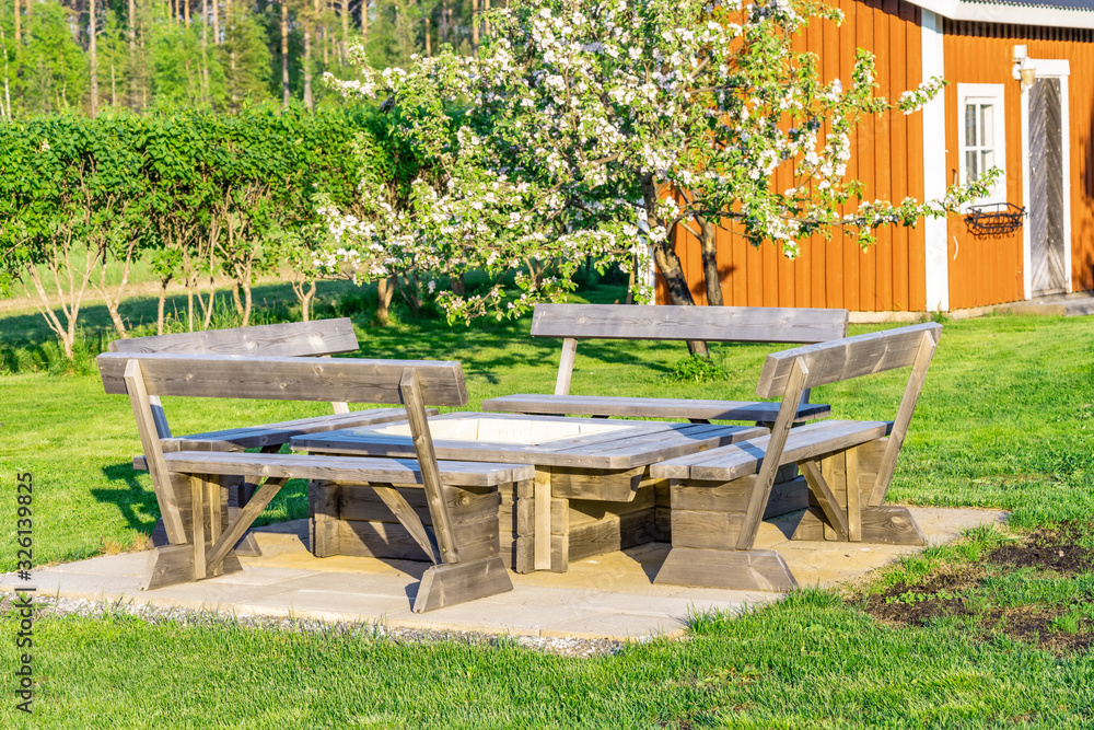 Stylish wooden barbeque spot with benches and table standing at concrete plates in the middle of green Swedish garden, middle summer time. Vasterbotten, Northern Sweden, Umea