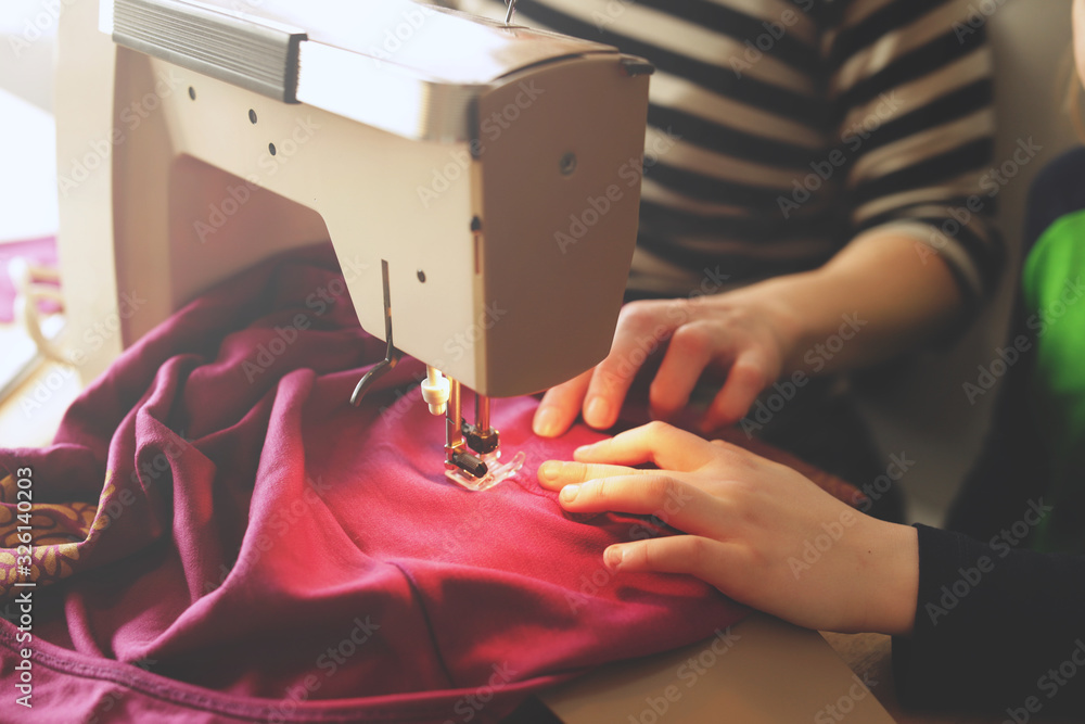 young girl repairs her pink skirt with a small sewing machine under supervision of her mother at home - sustainable fashion concept - obrazy, fototapety, plakaty 