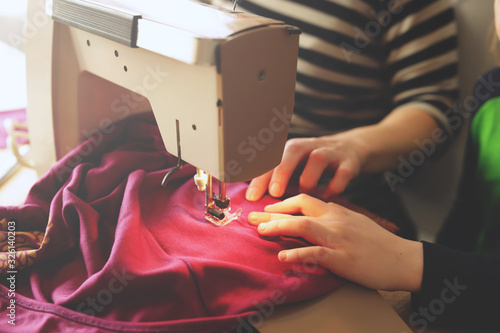 young girl repairs her pink skirt with a small sewing machine under supervision of her mother at home - sustainable fashion concept