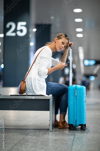 Young woman with her luggage at an international airport, waiting for her luggage to arrive at the baggage claim zone photo