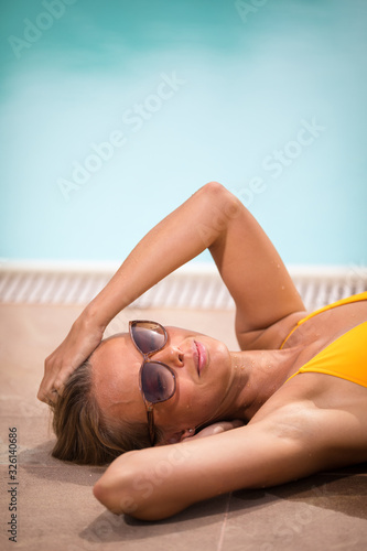Young Beautiful Suntanned Woman wearing sunglasses relaxing next to a Swimming Pool  on a lovely Summer Day