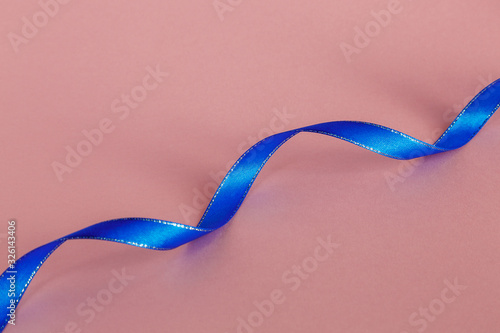 Blue satin ribbon on a pink background.  Selective focus. Space for text.