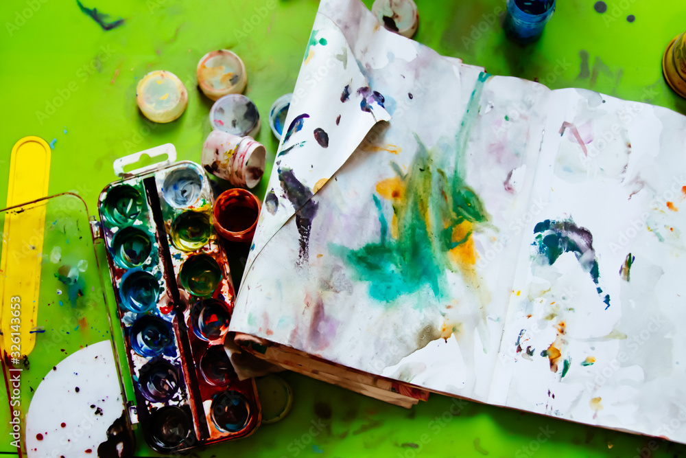 Fototapeta premium Dirty baby table with paints and album.The little child used all the paints and painted a masterpiece