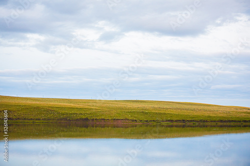 classic nature landscape with clear lake, green grass and clouds sky