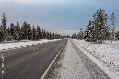 Empty highway surrounded by snow and evergreen trees bends around a corner on a clear morning