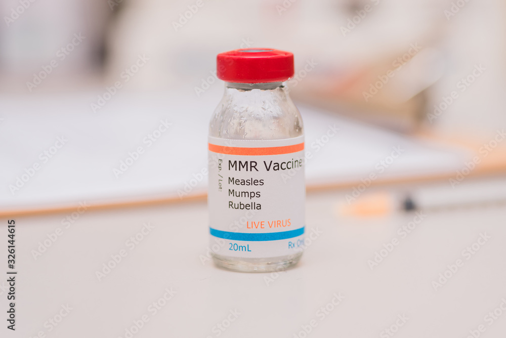 Measles mumps and rubella vaccine concept vial with patient chart and injection syringe in background Measles mumps and rubella vaccine concept vial with patient chart and injection syringe in background