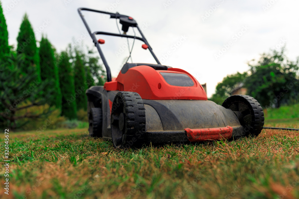 Obraz premium Lawn mower cutting green grass in backyard.Gardening background.