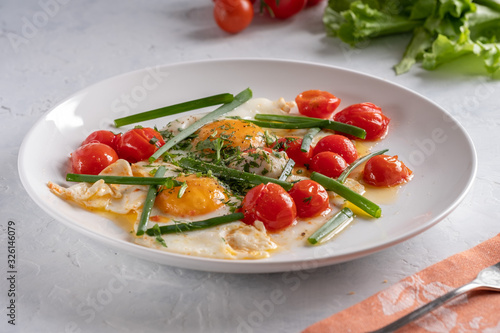 Fried eggs with cherry tomatoes and green onions on a white plate
