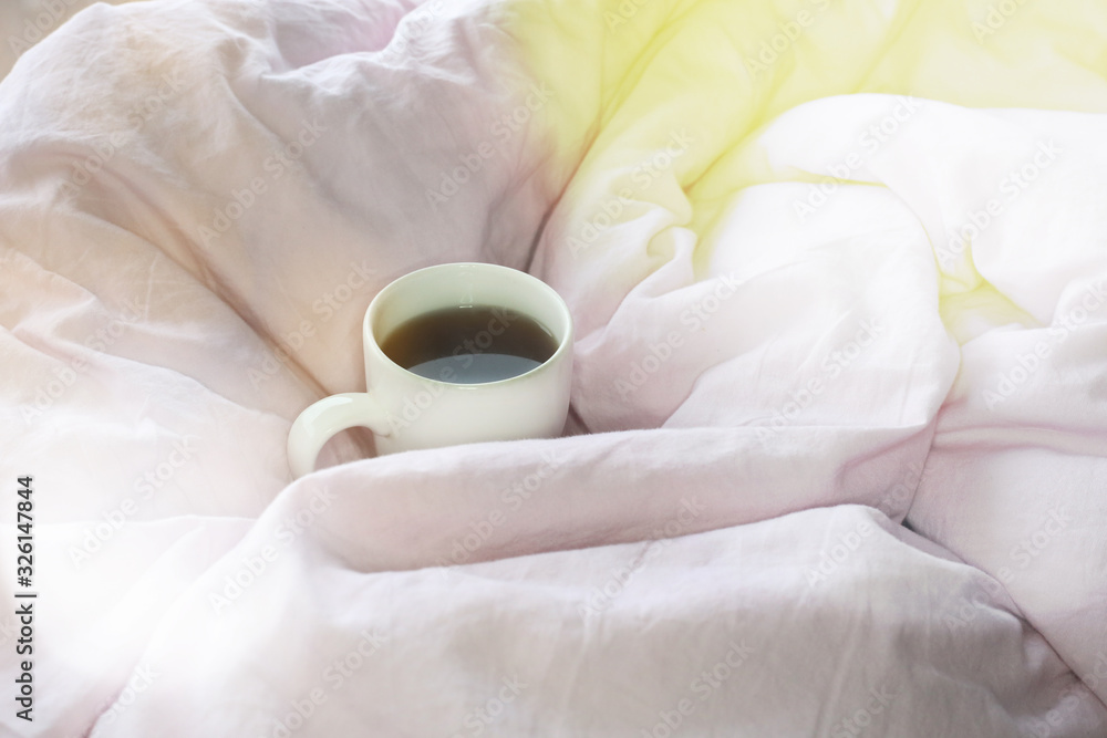 Morning coffee mug in pink bed sheet background. Cotton textile waved.