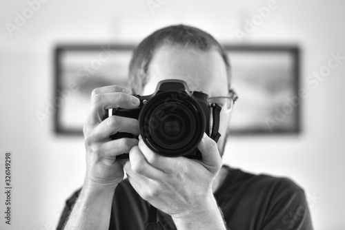 Self portrait through a mirror of an  unrecognizable caucasian man photographer holding a camera (focus on camera lens).