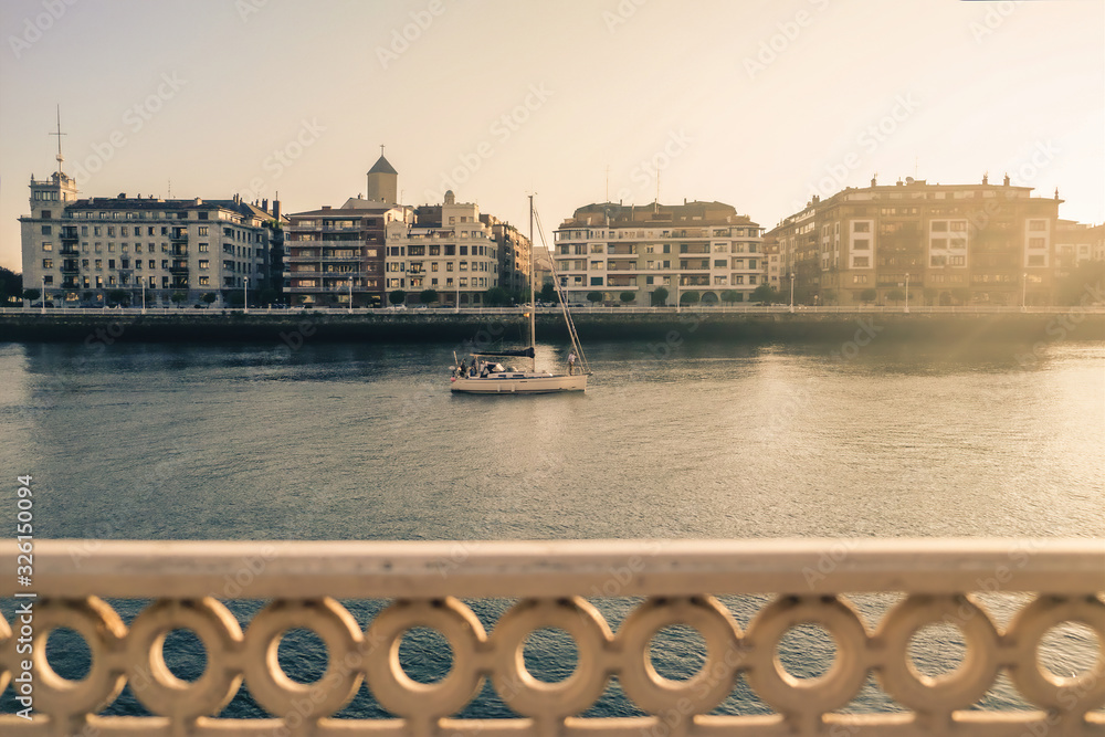 Obraz premium A sailboat sails a river in summertime in the city with a nice foreground