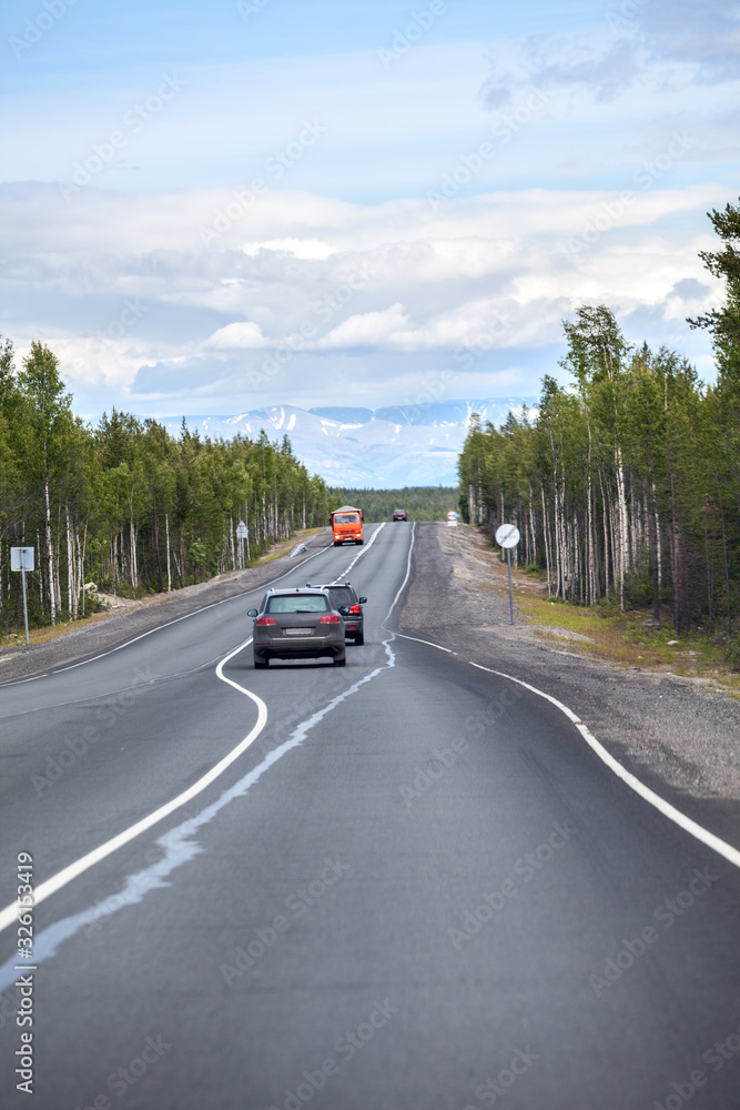 Highway stretches away to mountains on horizon. Passenger cars driving on the Kola asphalt road. It is way to the Murmansk city on north of Russia