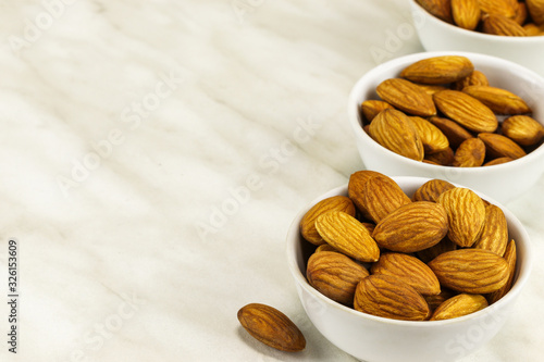 Almonds in three white bowls on a white marble surface on the right