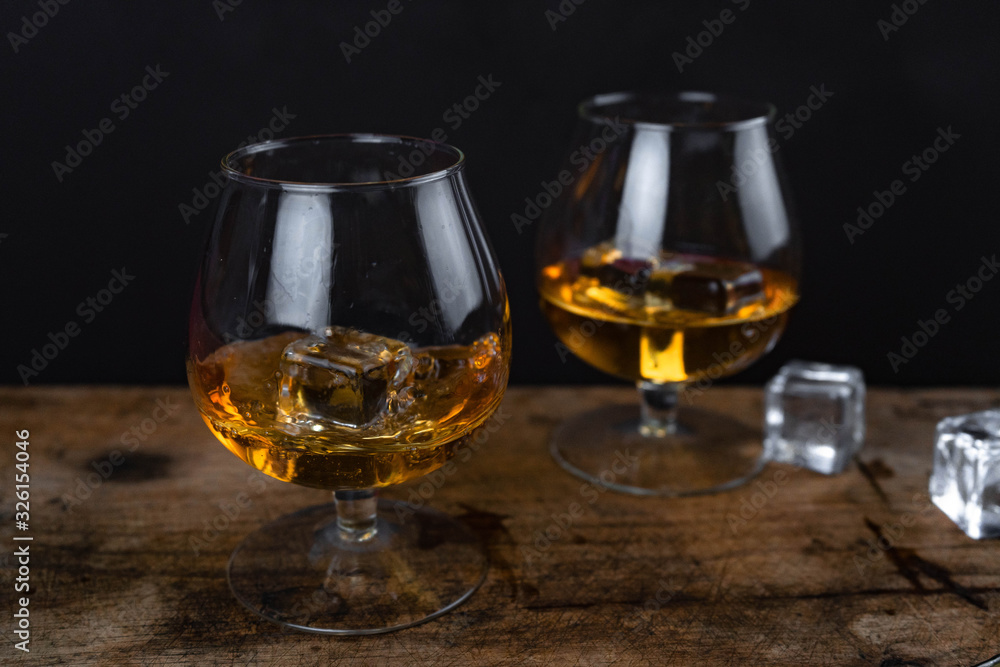 Two whiskey / cognac glasses with ice on a wooden background. Dark backdrop. Two whiskey / cognac glasses with ice on a wooden background. Dark backdrop.