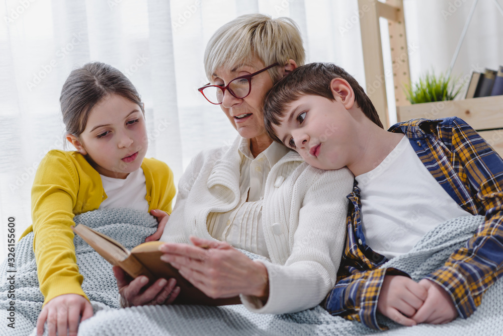 Grandmother reading a book to her grandchildren. Cute boy and girl spending time with her granny. 