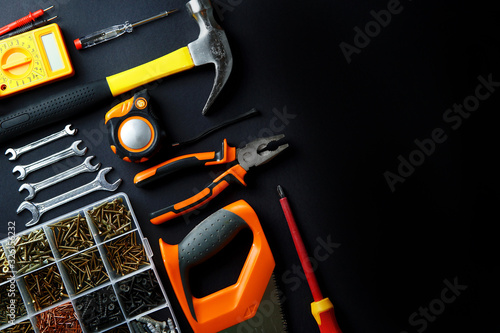 Construction tools for home renovation on black background. Hammer, hand saw, pliers, screwdriver, wrenches, tape measure, multimeter, screws. Maintenance, reparing concept. Place for text, flat lay. © Anna