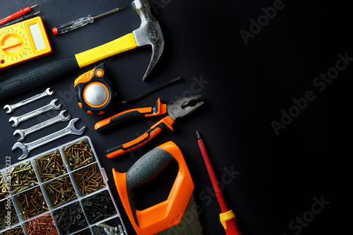 Construction tools for home renovation on black background. Hammer, hand saw, pliers, screwdriver, wrenches, tape measure, multimeter, screws. Maintenance, reparing concept. Place for text, flat lay.