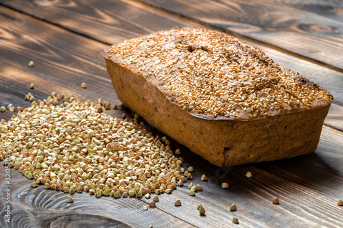 Useful buckwheat bread with a golden crust and a bunch of green grains nearby on a wooden table. Vegan and vegetarian food. Delicious pastries made from natural ingredients. The whole loaf. Close up